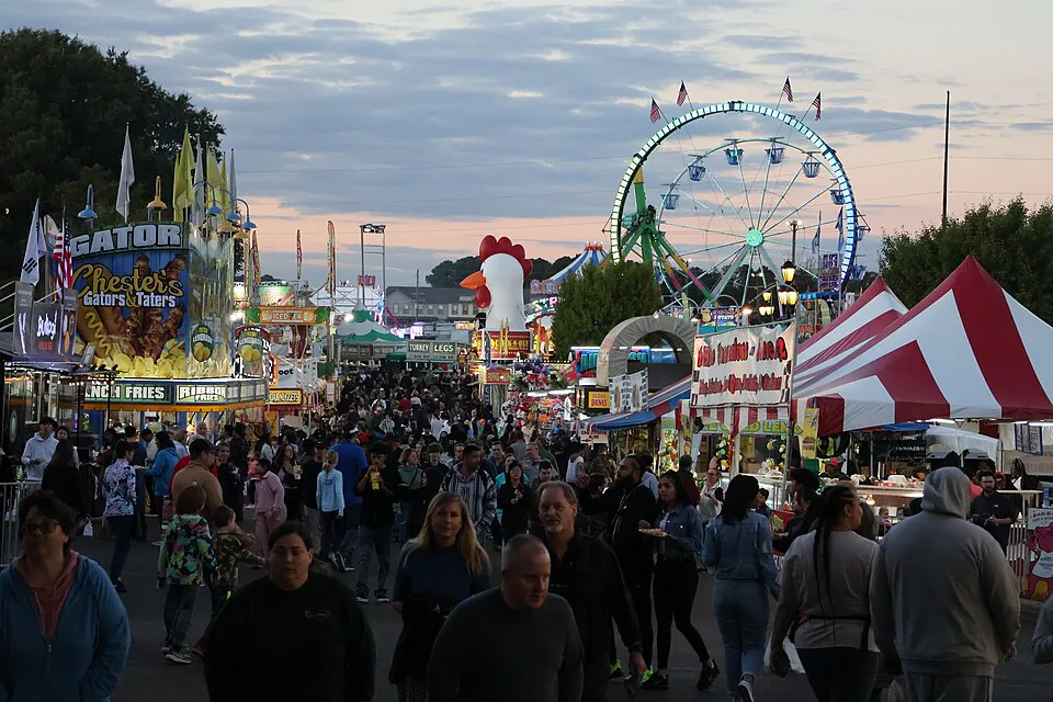 Crowds walking between food stands and a Ferris wheel at the North Carolina State Fair